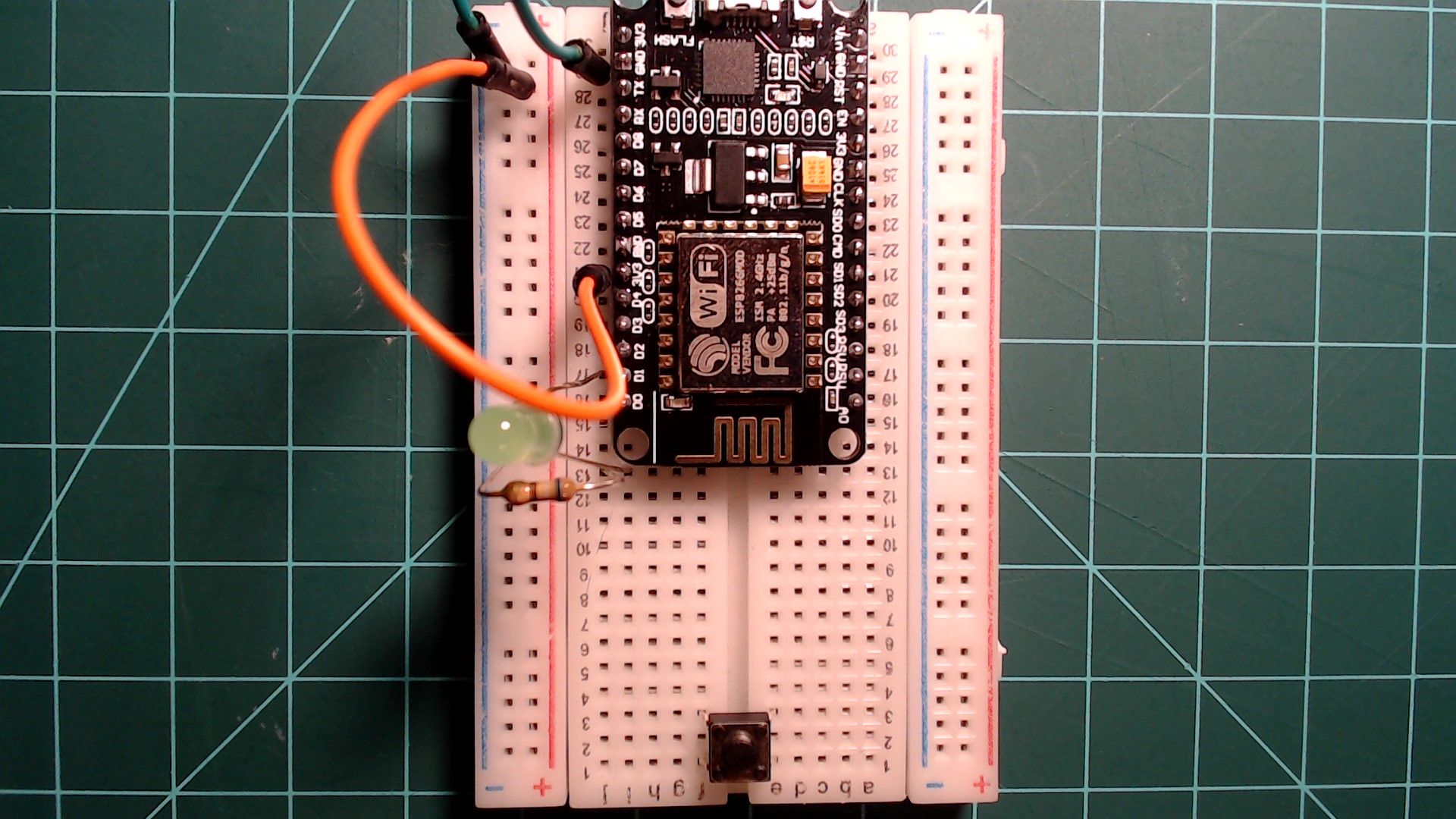 The LED circuit with a push button added at the far end of the breadboard across the centre gap, and an orange wire from a 3V3 pin of the NodeMCU to the rail beside the ground rail.