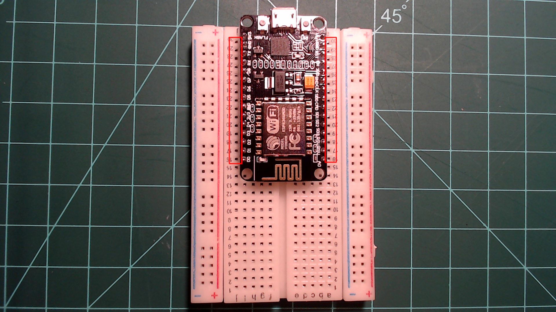A NodeMCU pressed into a breadboard across its centre gap, USB port at the top, with red boxes showing one free column of holes left beside each row of pins.