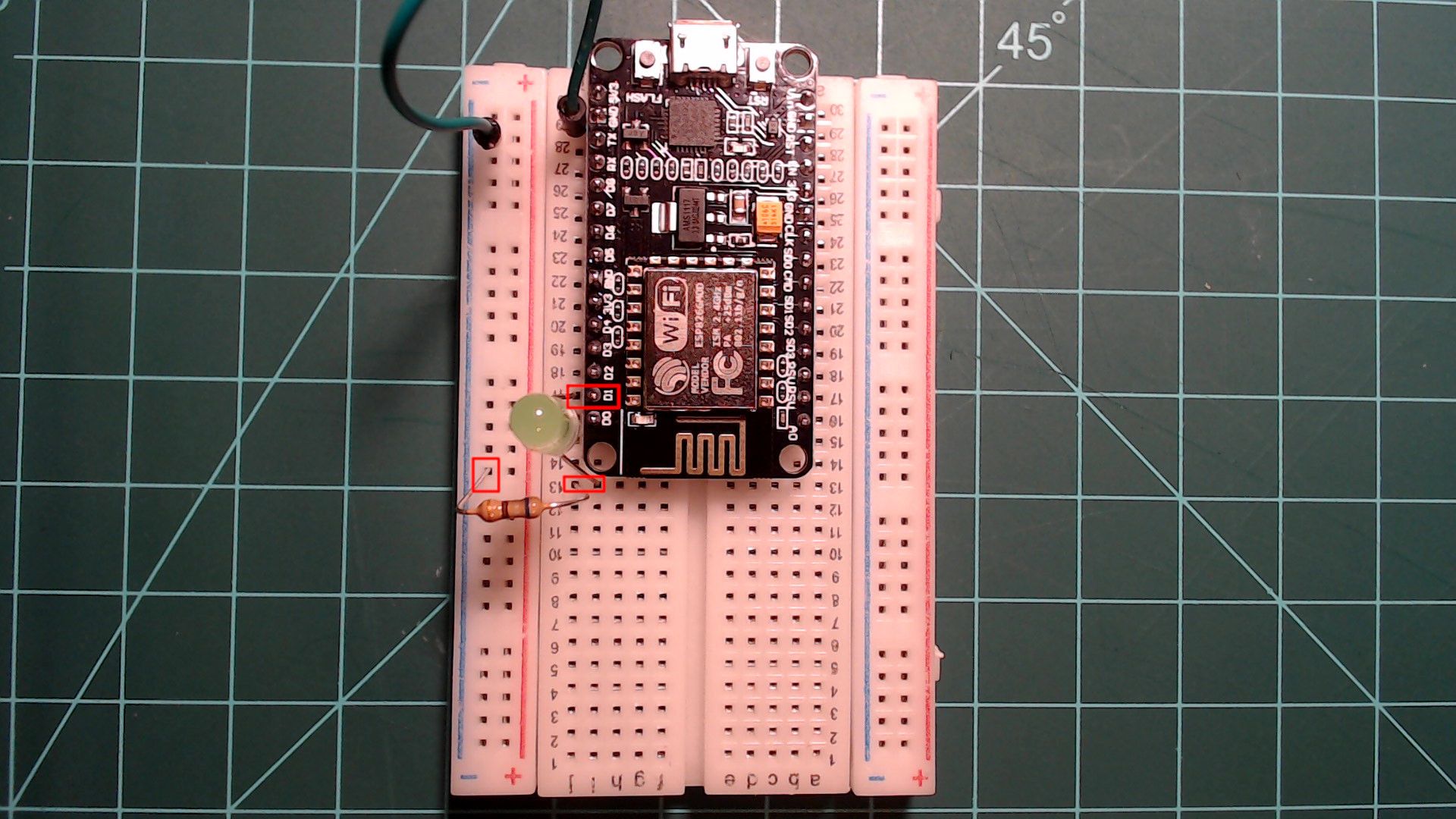 The NodeMCU on the breadboard with an LED whose long leg sits beside the D1 pin and short leg in an empty row below, and a resistor from that row to the ground rail, each spot outlined in red.