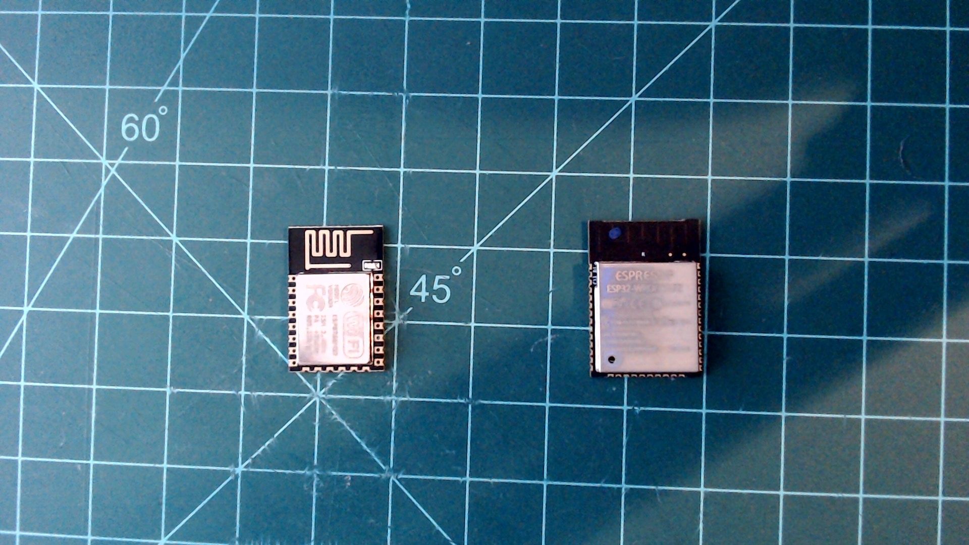 Two bare modules on a cutting mat: on the left the smaller ESP8266, with a zigzag antenna above its metal shield, and on the right the larger ESP32, its shield marked 'Espressif ESP32'.