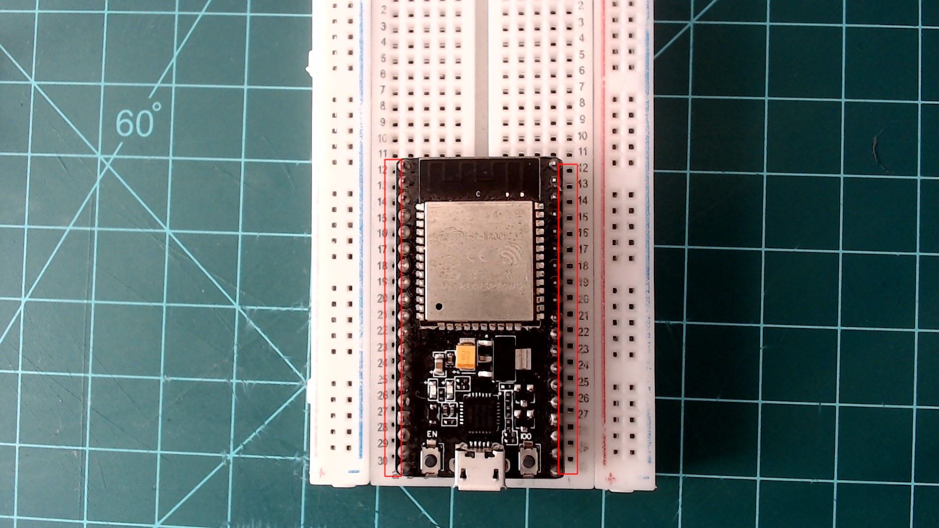 An ESP32 NodeMCU pressed into a breadboard across its centre gap, USB port at the bottom, with red boxes showing one free column of holes beside each row of pins.