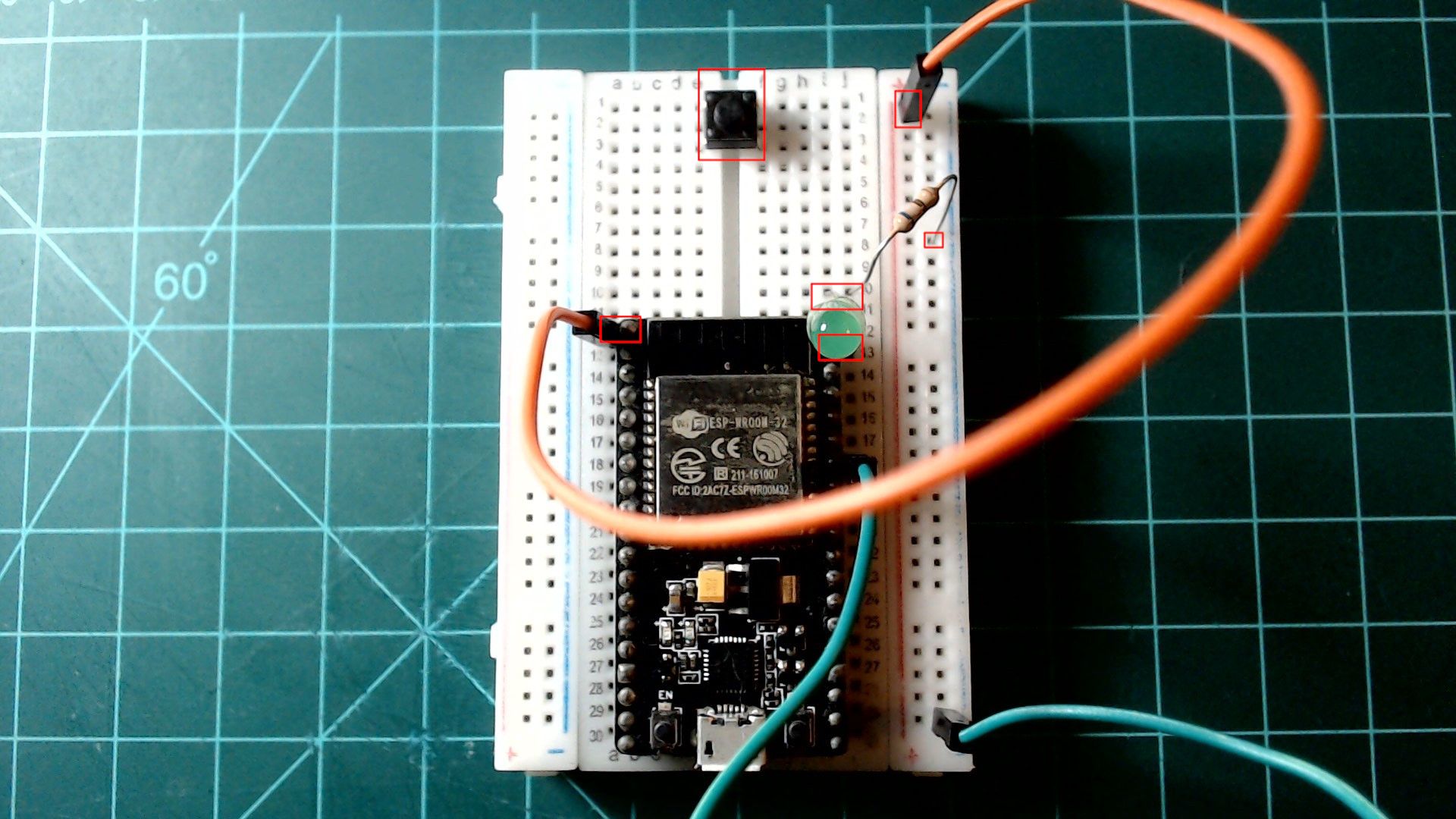 The circuit from the previous picture, now with a push button added at the far end of the breadboard across the centre gap, and an orange wire from the board's 3V3 pin, top left, to the inner rail on the right; each addition is outlined in red.