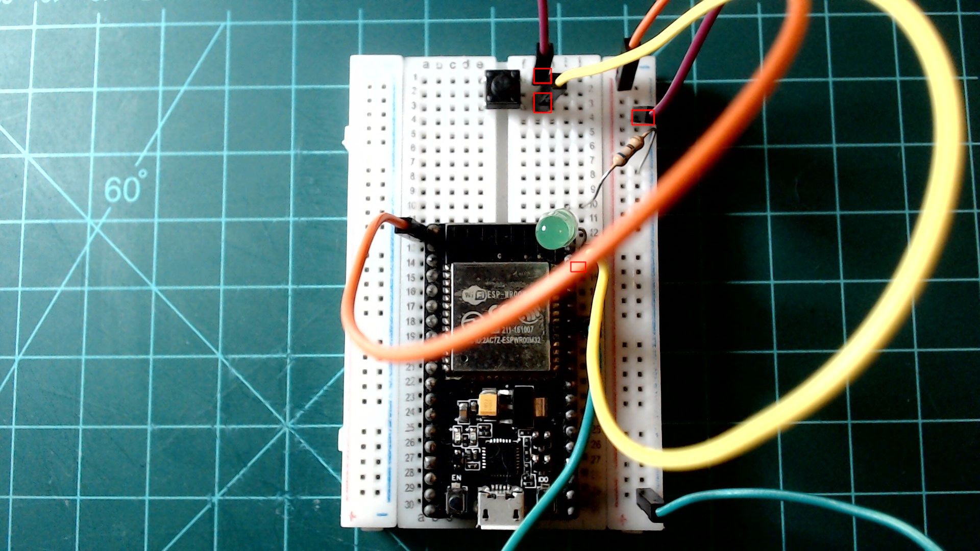 The circuit from the previous picture, now with the button wired in: a yellow wire from the GPIO22 pin on the board's right side to one side of the button, and a purple wire from the other side to the ground rail, the ends outlined in red.