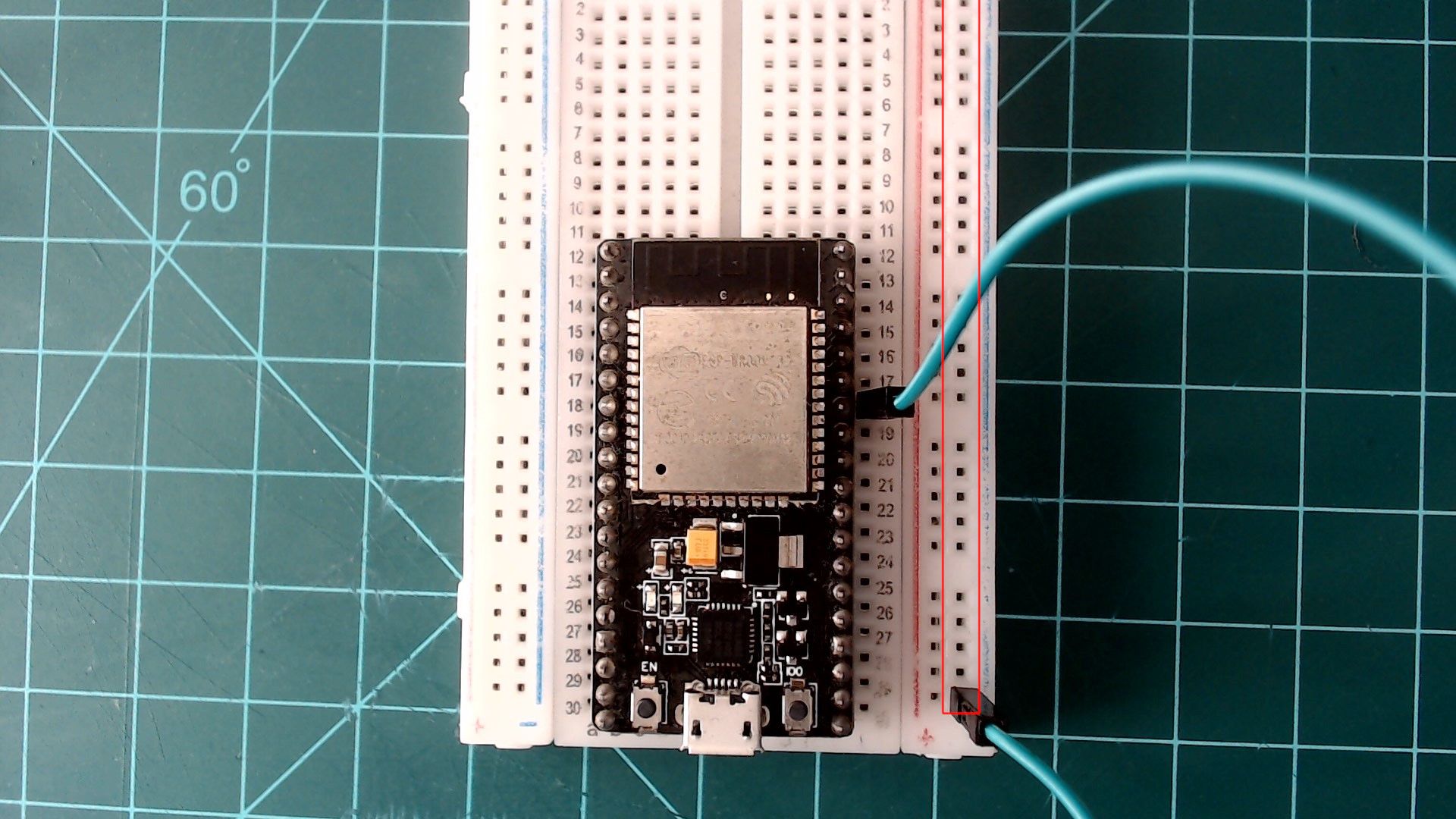 The ESP32 NodeMCU on the breadboard with a green jumper wire from a GND pin on its right side to the outermost rail on the right, which is outlined in red.