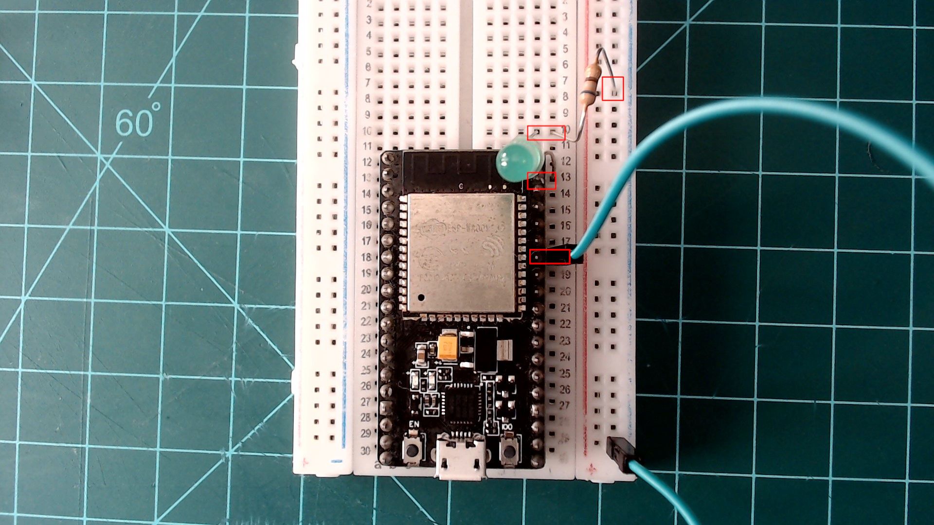 The ESP32 NodeMCU on the breadboard with a green wire from a GND pin on its right side to the ground rail, the outermost rail on the right. An LED sits by the board's top right corner, its long leg next to the GPIO23 pin and its short leg in an empty row above, and a resistor joins that row to the ground rail; each spot is outlined in red.