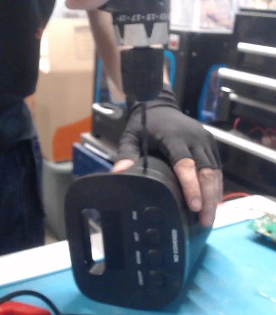 A gloved hand steadies the heater on its side while a cordless drill bores a hole in the casing beside the button panel.