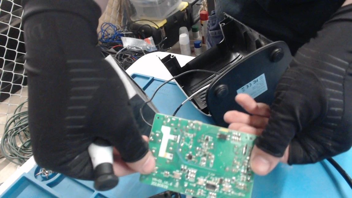 Gloved hands hold up the circuit board, showing its green underside with its small surface-mounted parts, in front of the empty enclosure.