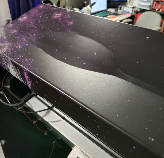 The cabinet's top edge, wrapped in a dark speckled space print, has a broad raised ripple where the wrap has lifted away from the metal.
