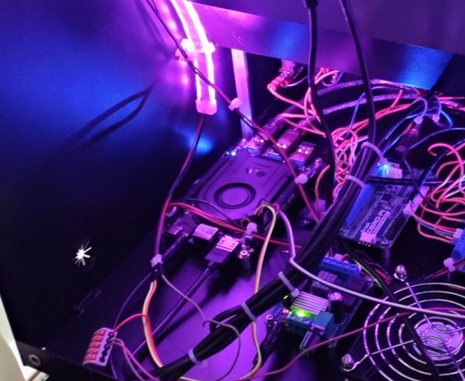Inside the cabinet, lit purple by an LED strip, a circuit board with a cooling fan and USB ports sits among bundles of cable-tied wires, small driver boards and a fan grille.