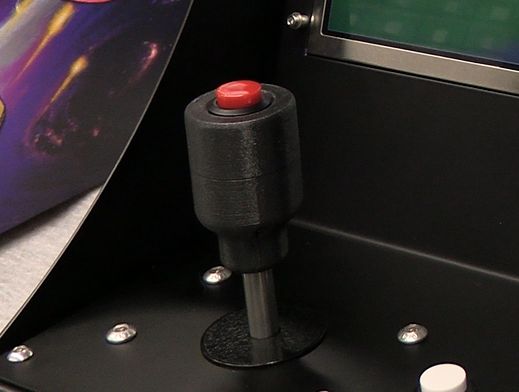 A short metal joystick shaft on the cabinet's control panel, topped with a black cylindrical grip that has a red arcade button set into its top.